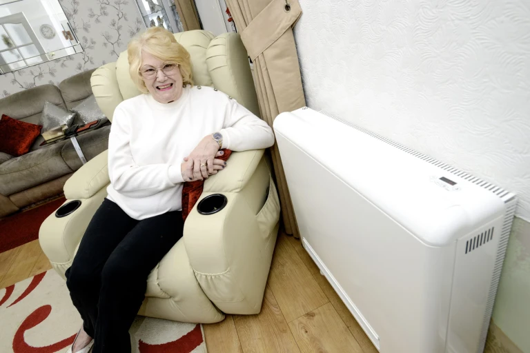 Ann smiling, sitting in an armchair next to a storage heater