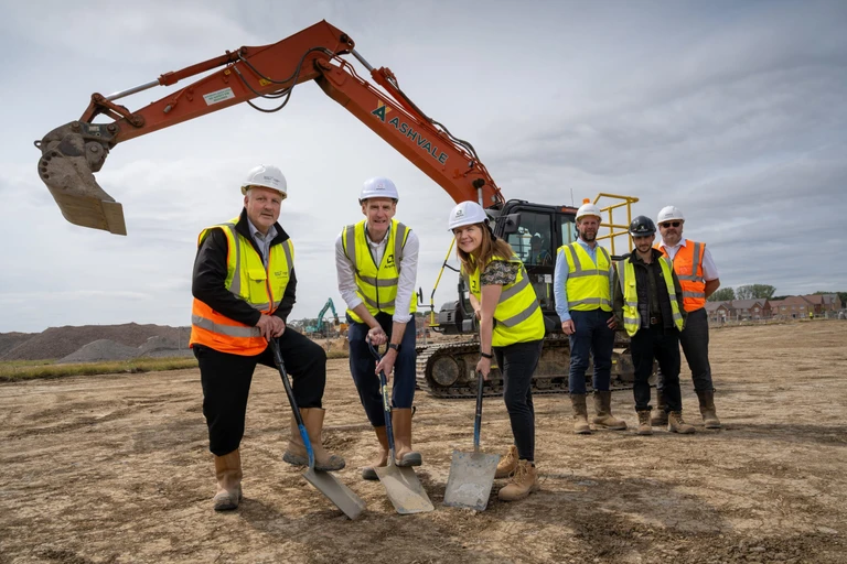 Representatives from Amplius and Vistry in hard hats and hi vis vests breaking the ground at Wixams with a mechanical digger in the background