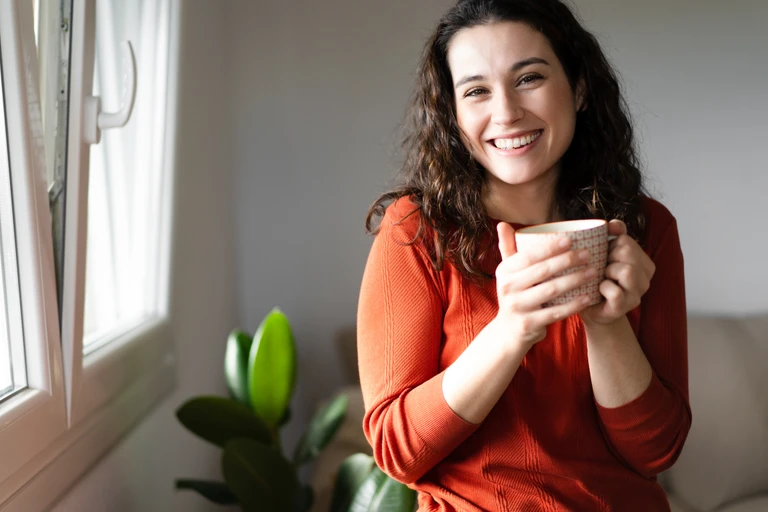 Happy young beautiful woman having a coffee or tea at home
