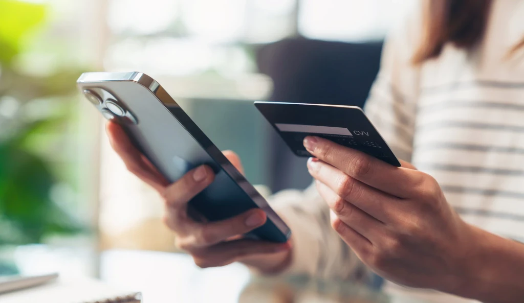 Woman's hand holding a bank card and using smartphone to make a payment