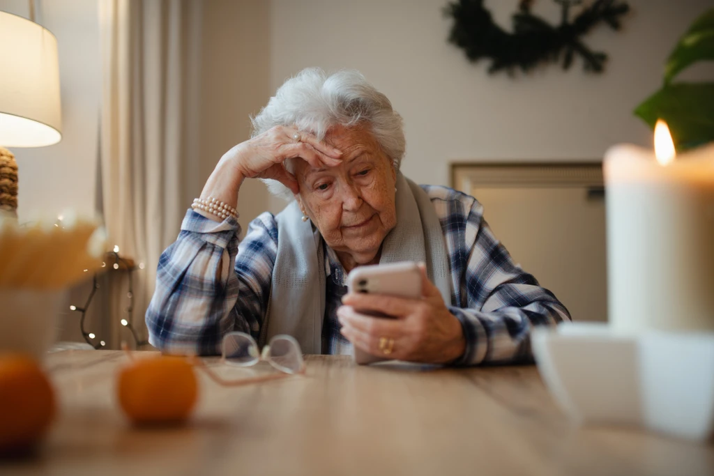 Elderly woman struggling to use smartphone, looking confused.