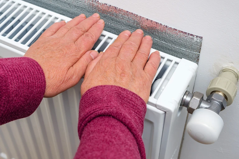 Elderly woman warming her frozen hands on a heater. Close-up, selective focus.