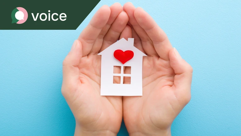 Hands holding a cut out shape of a house with a heart on it