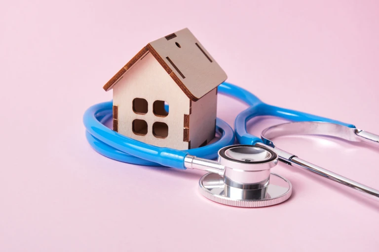 Medical stethoscope and toy house on a pink background