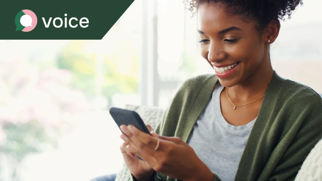 A young woman, sat in her home and smiling while using her mobile phone