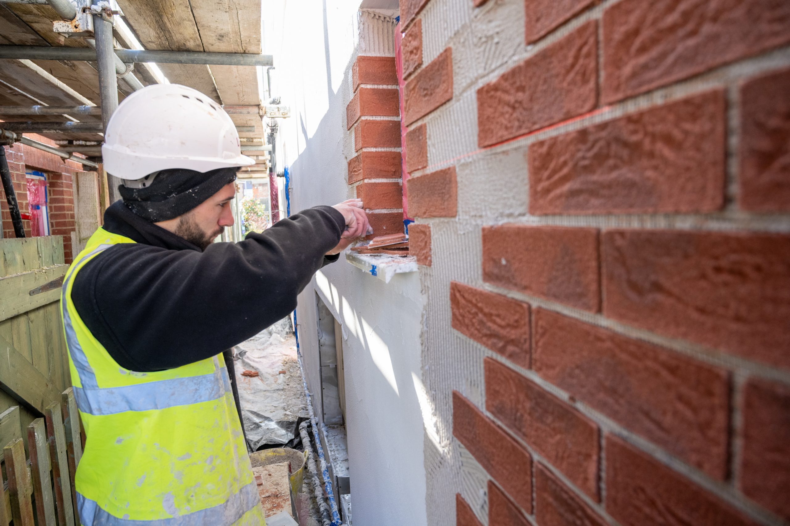 An operative in a hard hat affixing brick slips to a newly insulated wall