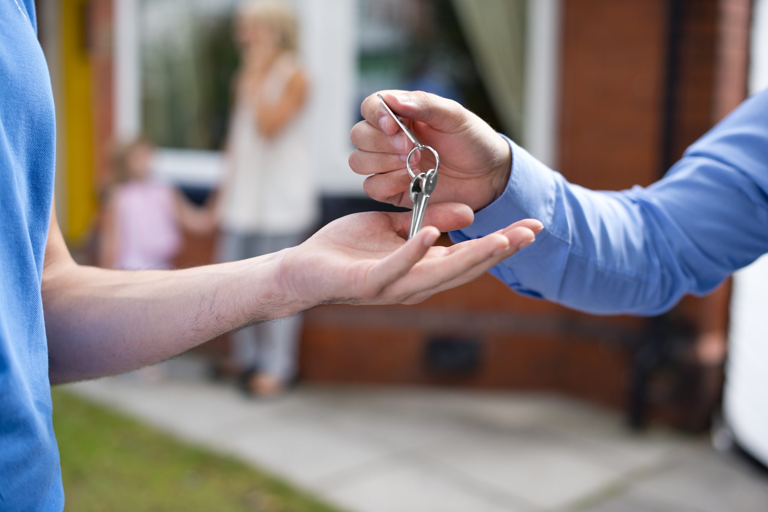 A person handing over keys to another person outside a house
